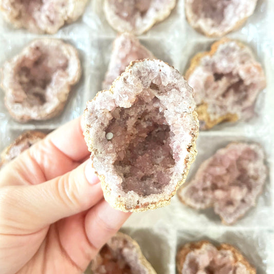 Close-up of a hand holding a crystal geode with more geodes in the background.