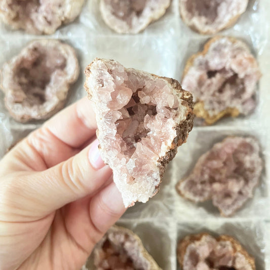 Hand holding a pink crystal geode with more geodes in the background